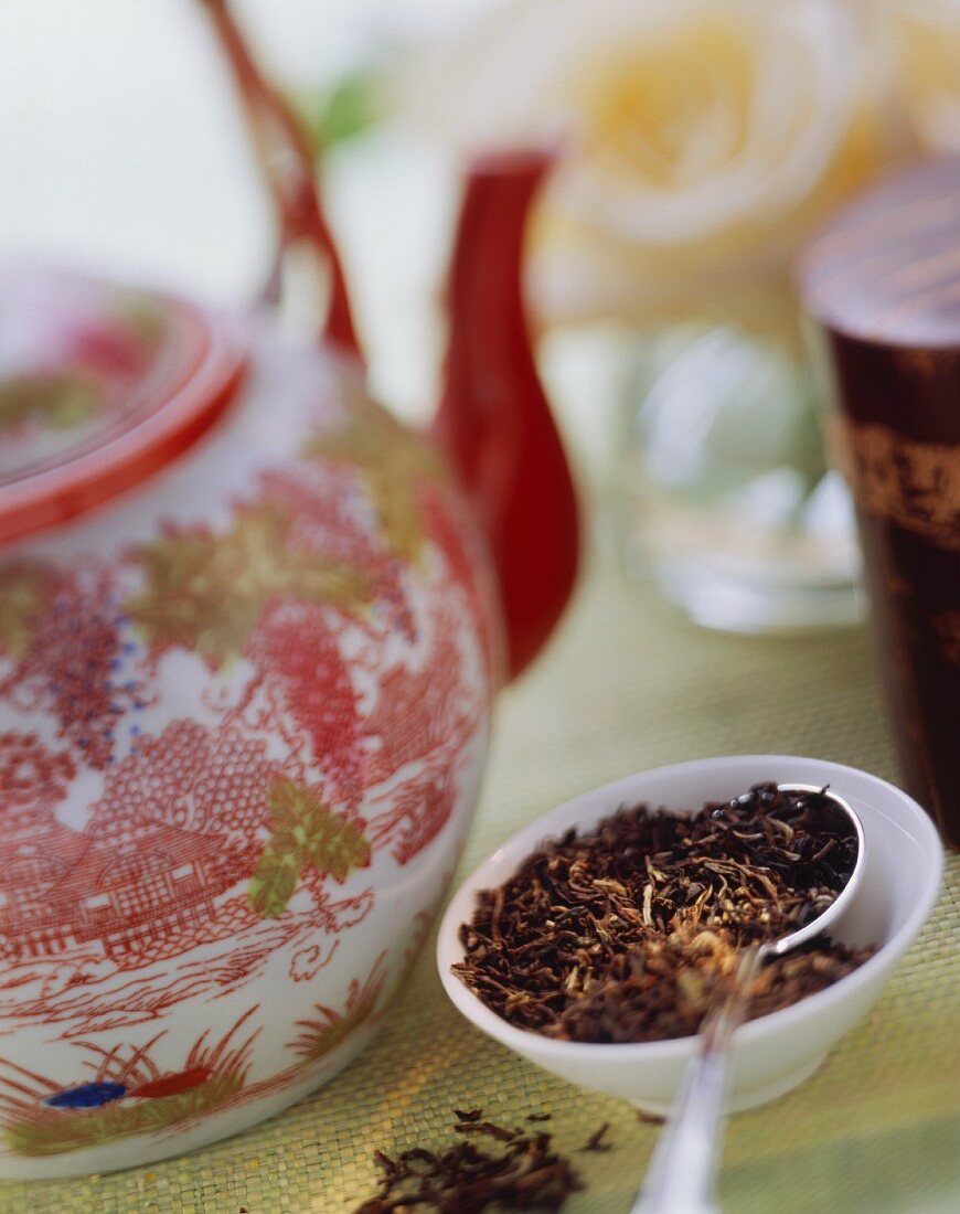 Black tea leaves beside Asian teapot