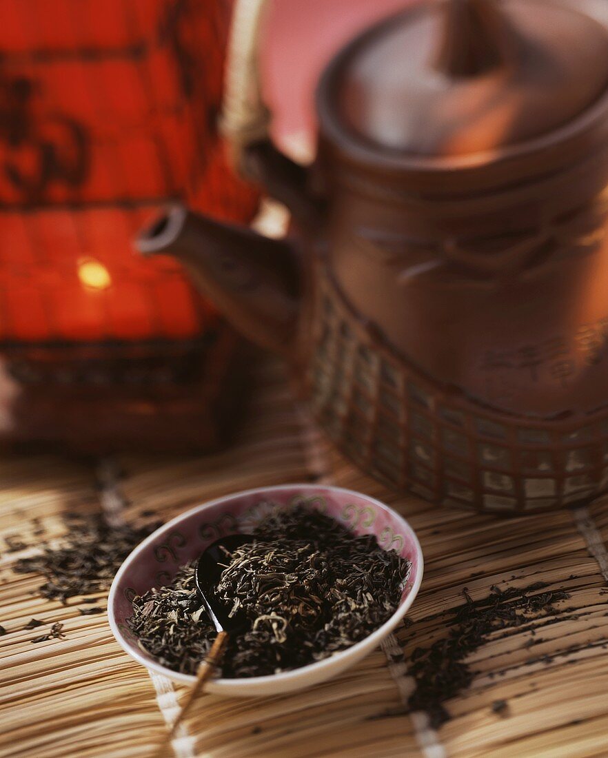 Schwarze Teeblätter im Schälchen, dahinter eine Teekanne