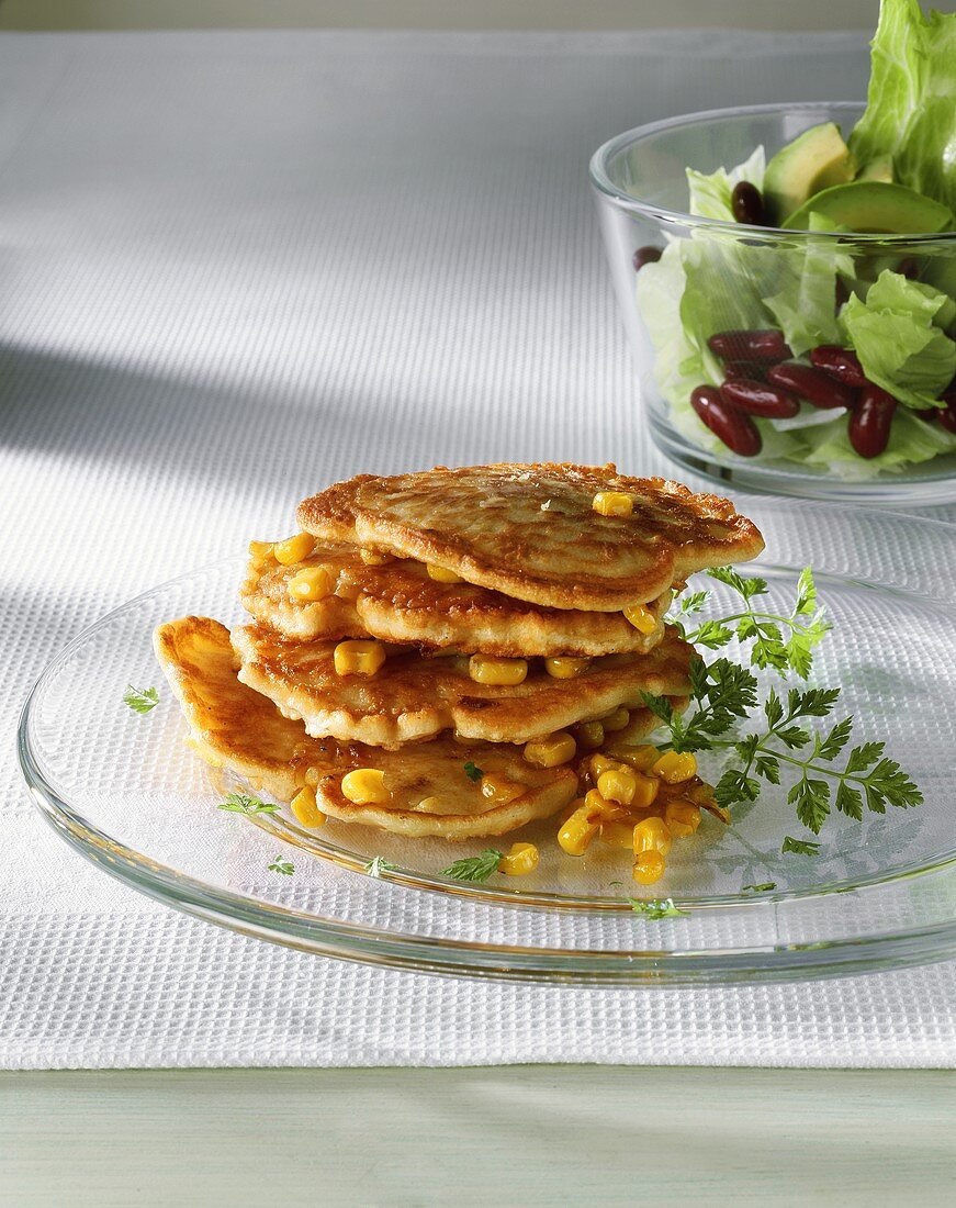 Corn pancakes on top of each other, lettuce in bowl behind