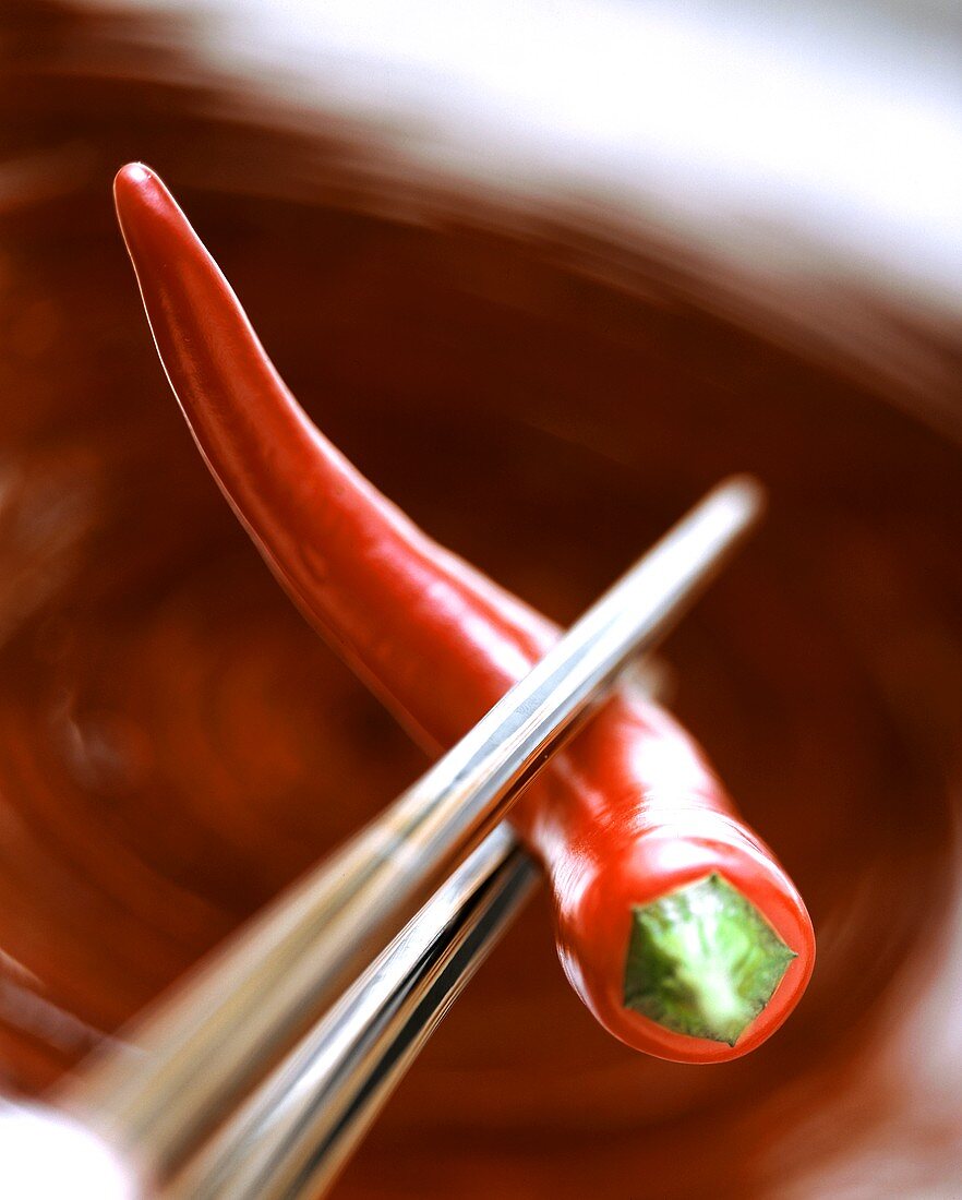 Chopsticks holding a red chili pepper