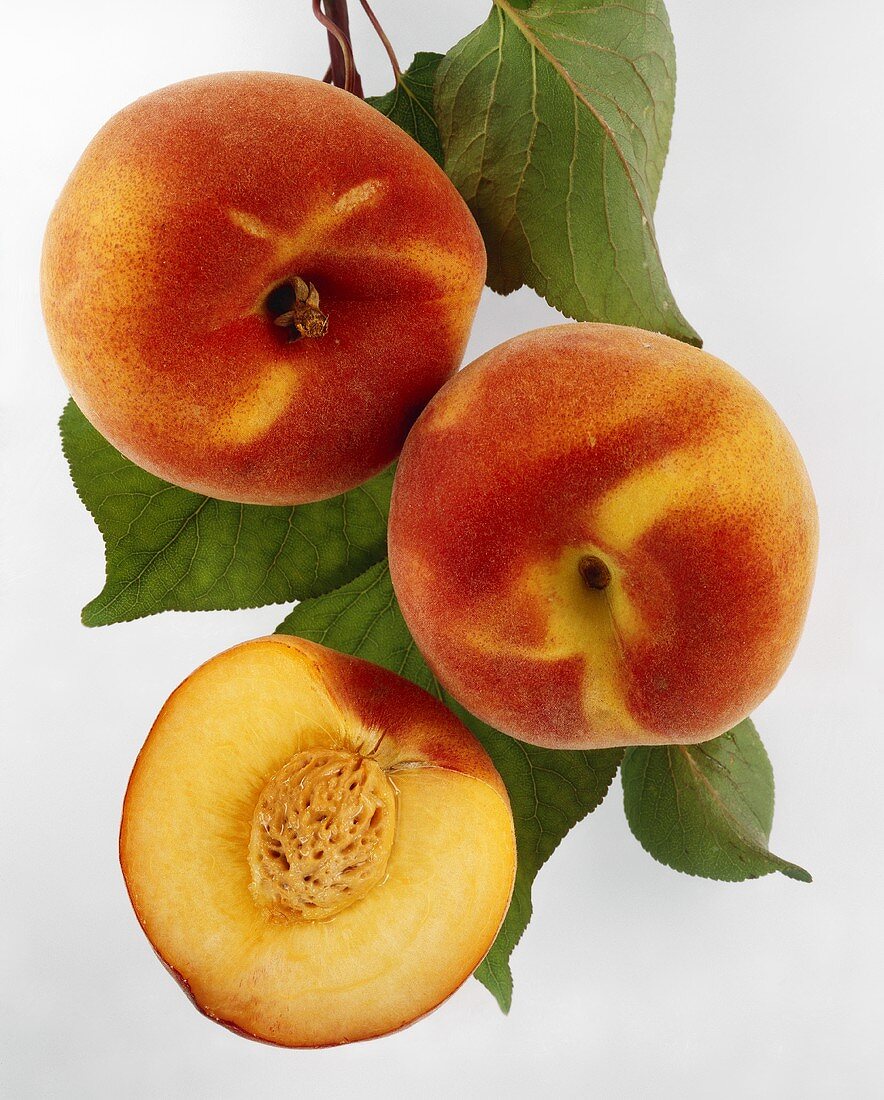 Half a peach and two whole peaches with leaves