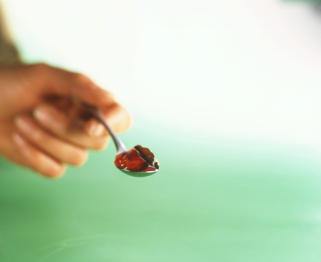 Hand hält Löffel mit Marmelade