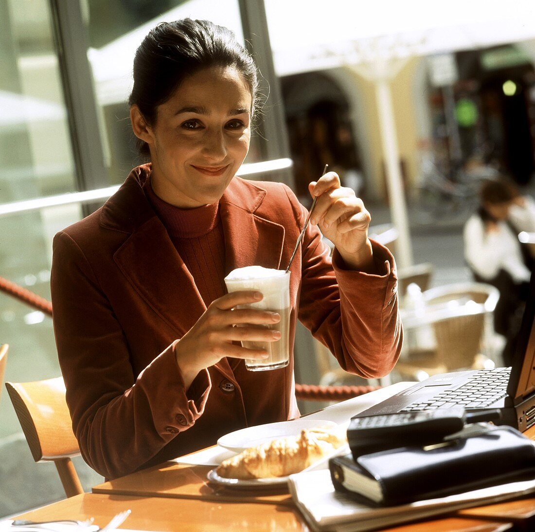 Junge Frau mit Latte Macchiato sitzt vor Laptop im Café