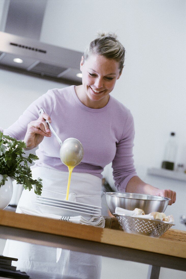 Young woman ladling soup into plate