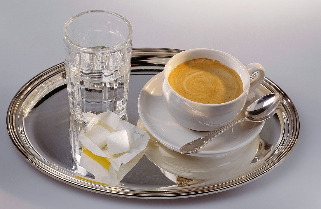 Cup of coffee, glass of water & sugar cubes on silver tray