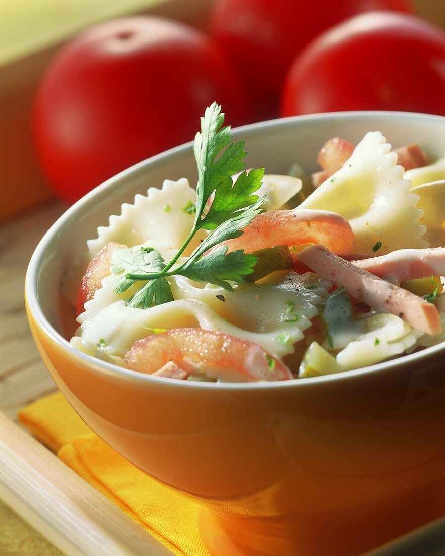 Pasta salad with tomatoes and strips of ham in bowl