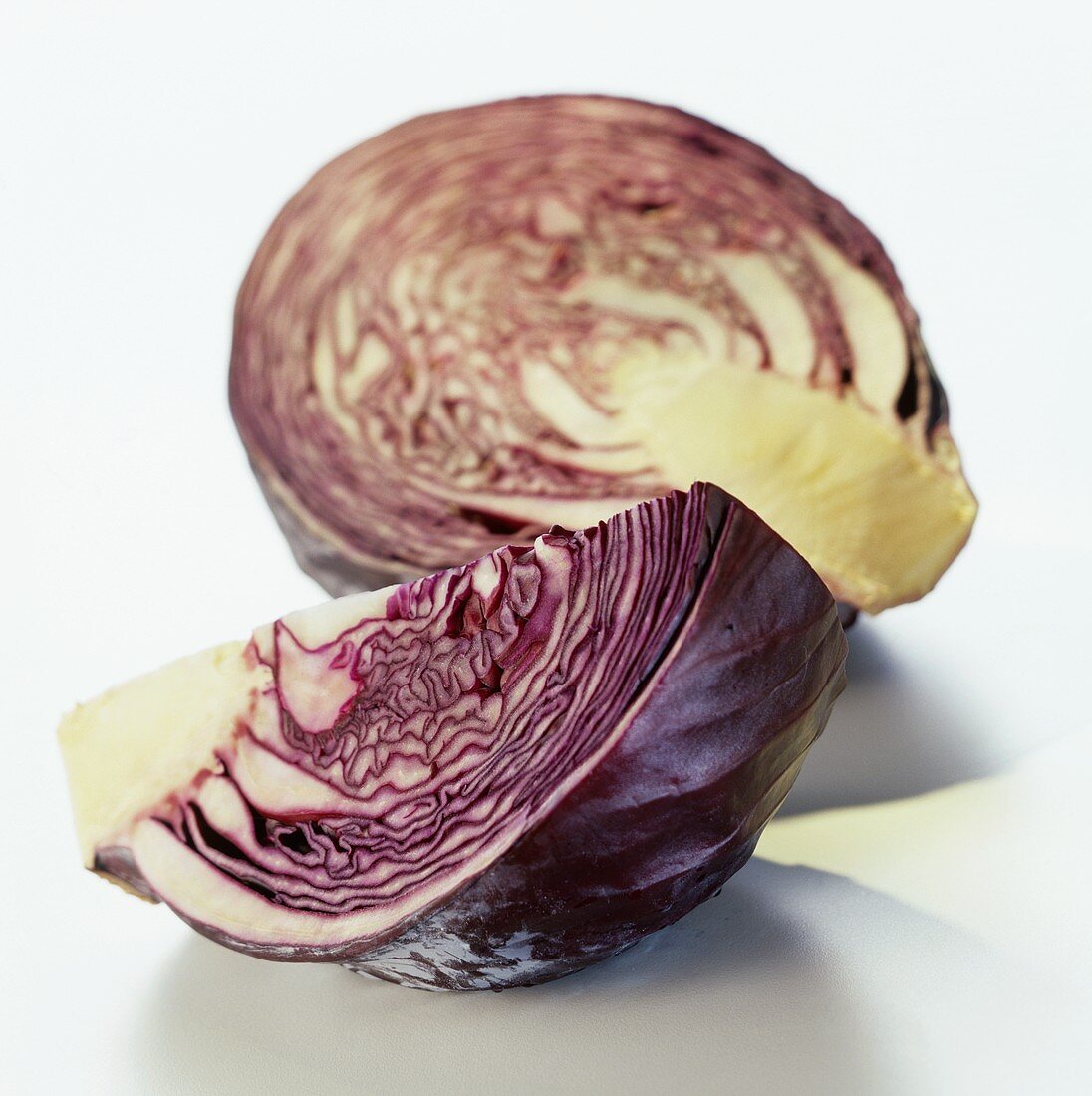 A quarter of a red cabbage lying in front of half a cabbage