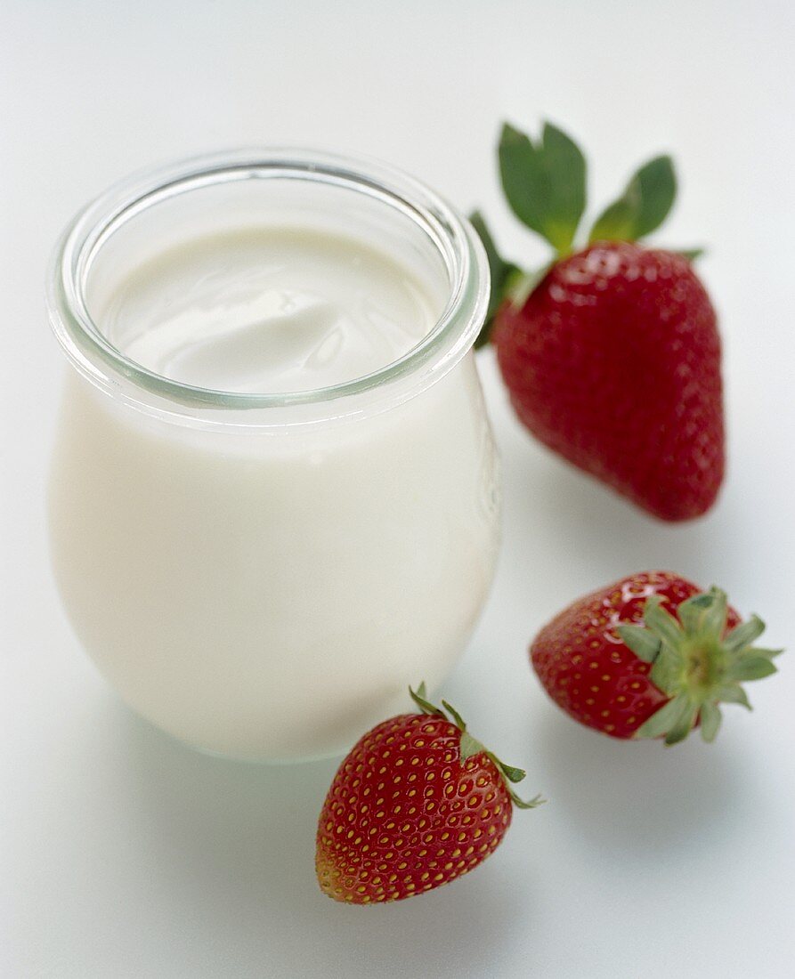 Ein Glas Naturjoghurt, daneben frische Erdbeeren