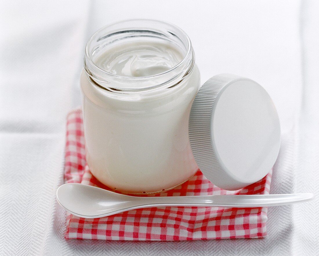 A jar of yoghurt with spoon on pink checked cloth