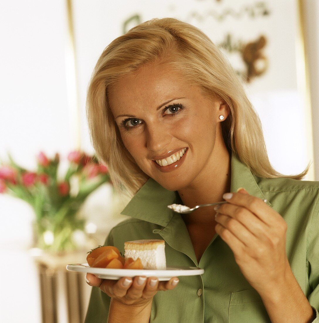 Frau hält Teller mit einem Stück Torte & Aprikosenspalten