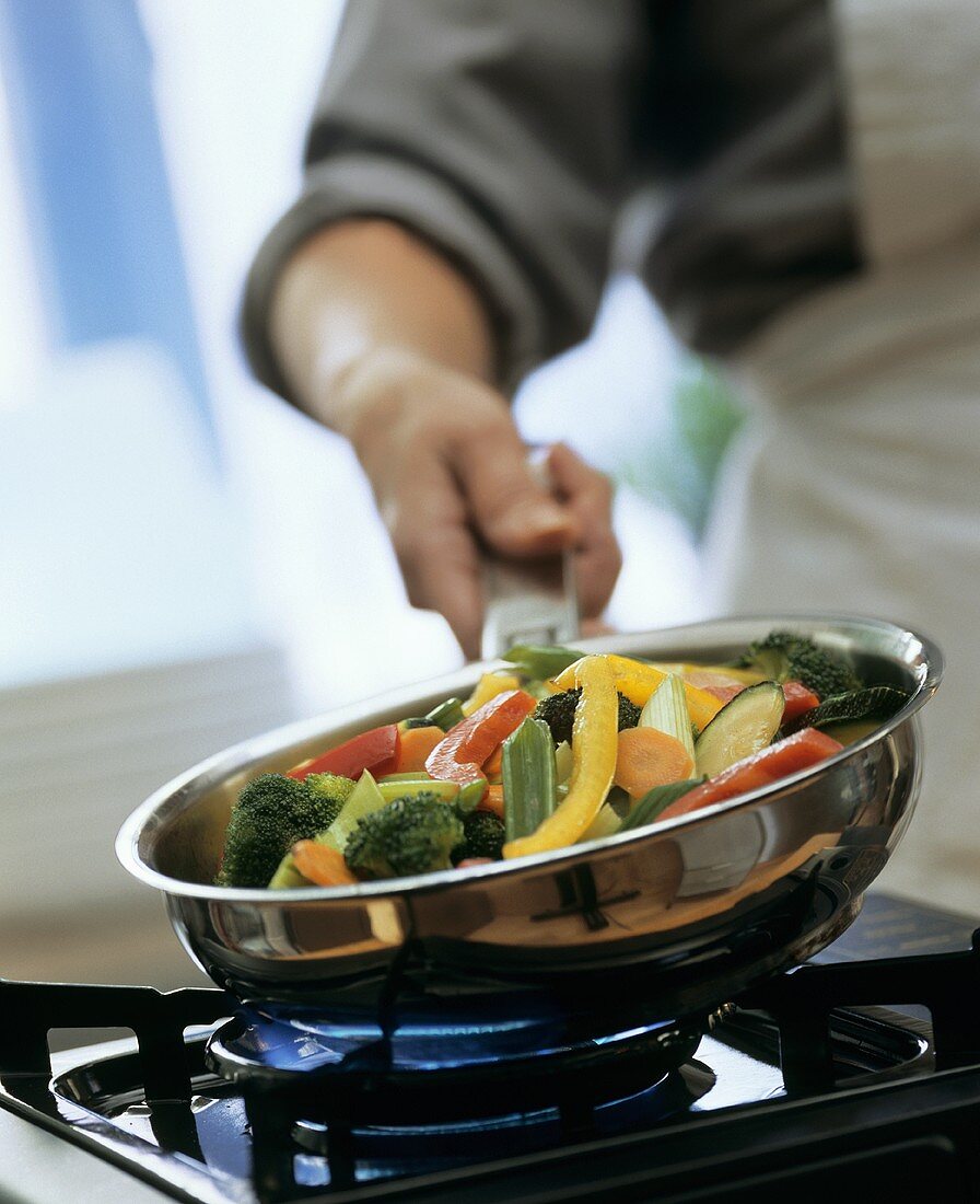 Vegetables being tossed in pan above cooker