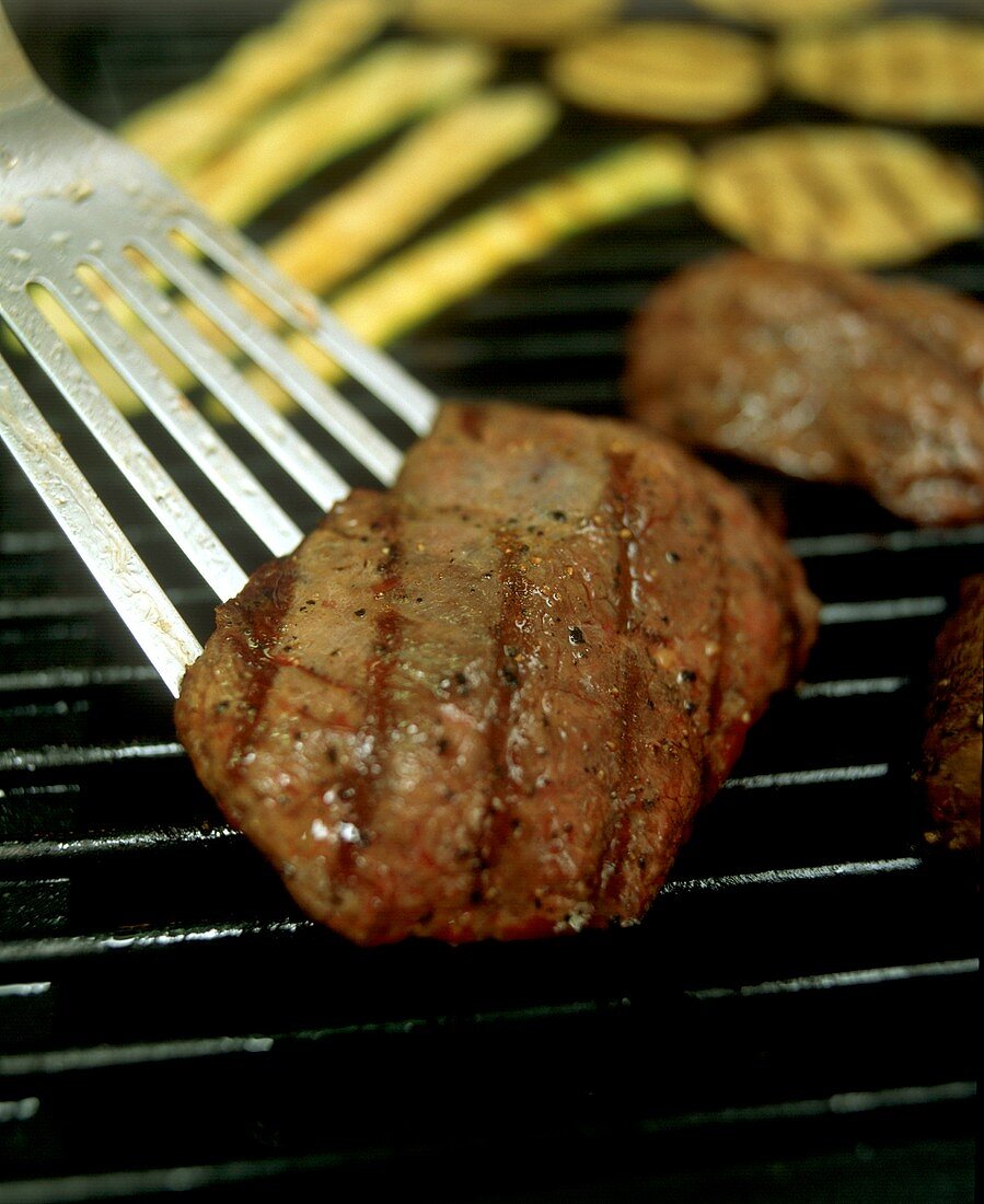 Steak auf dem Grill wird mit Pfannenwender gewendet