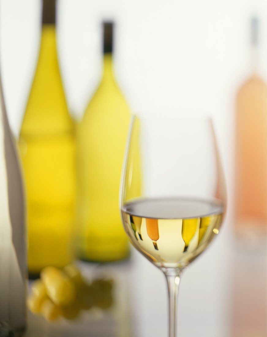 Ein Glas Weißwein und Weinflaschen im Hintergrund