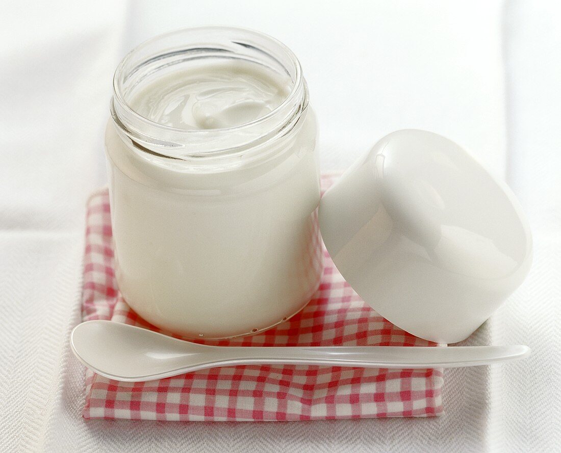Ein Glas Joghurt mit Plastiklöffel auf kariertem Tuch