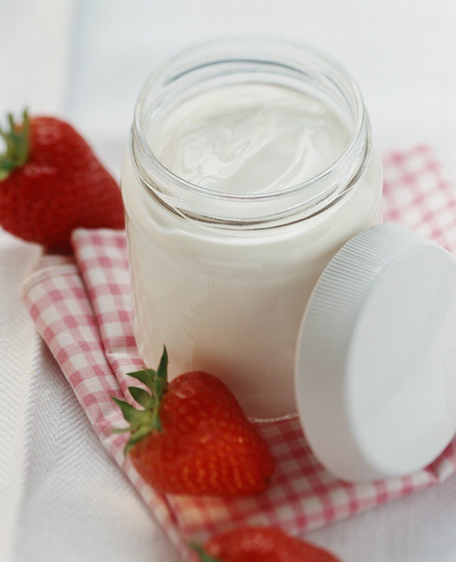 A jar of yoghurt, fresh strawberries beside it