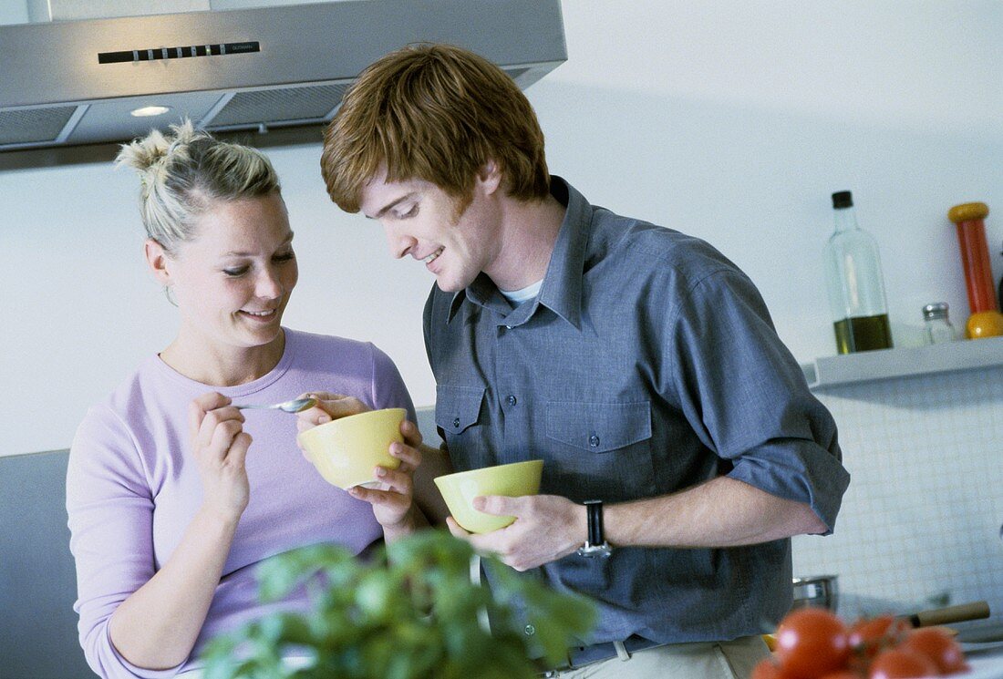 Young couple eating soup out of bowls (standing)
