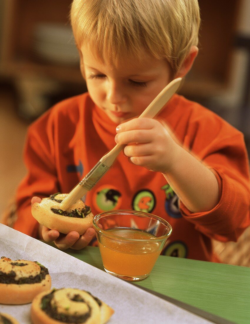 Small boy brushing poppy seed snails with apricot jam