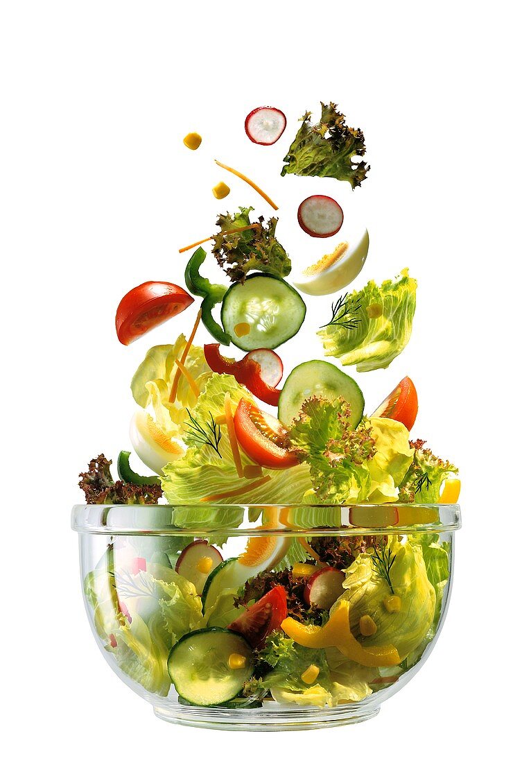 Frische Salatzutaten fallen in eine Glasschüssel