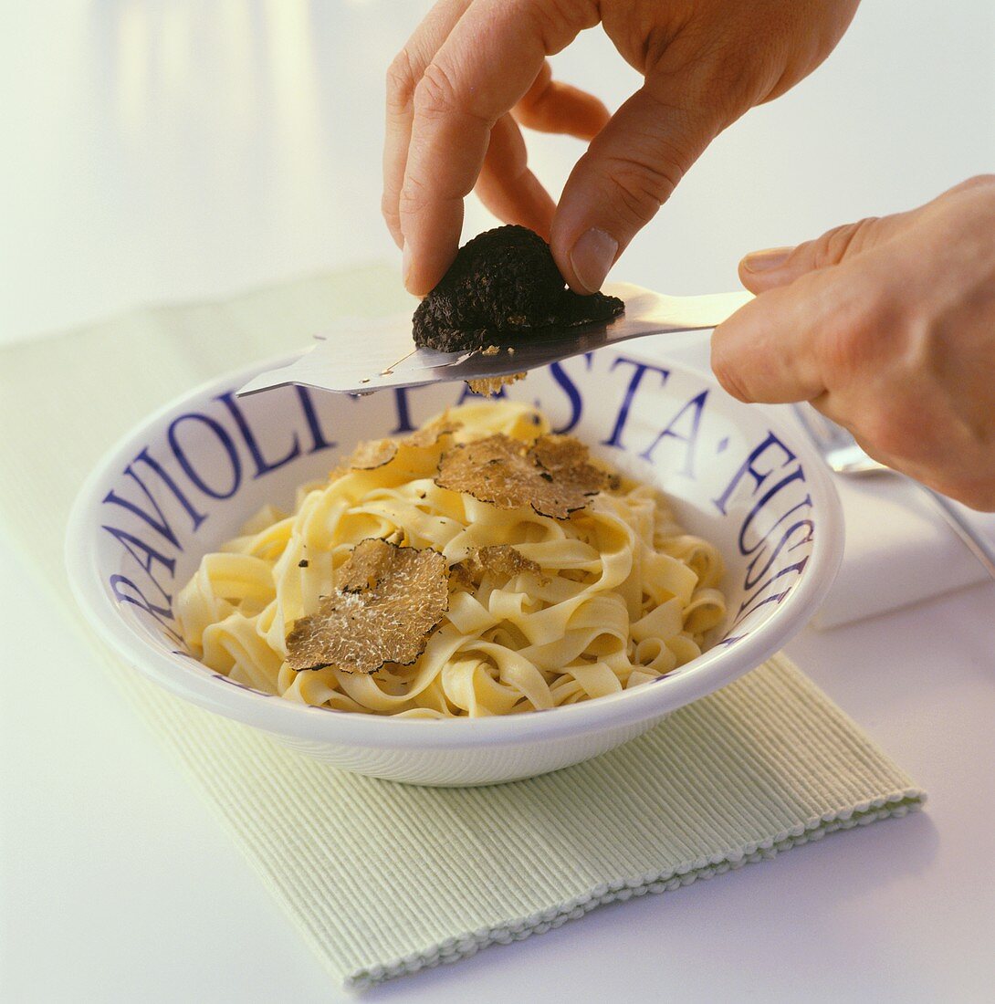 Slicing black truffle over tagliatelle