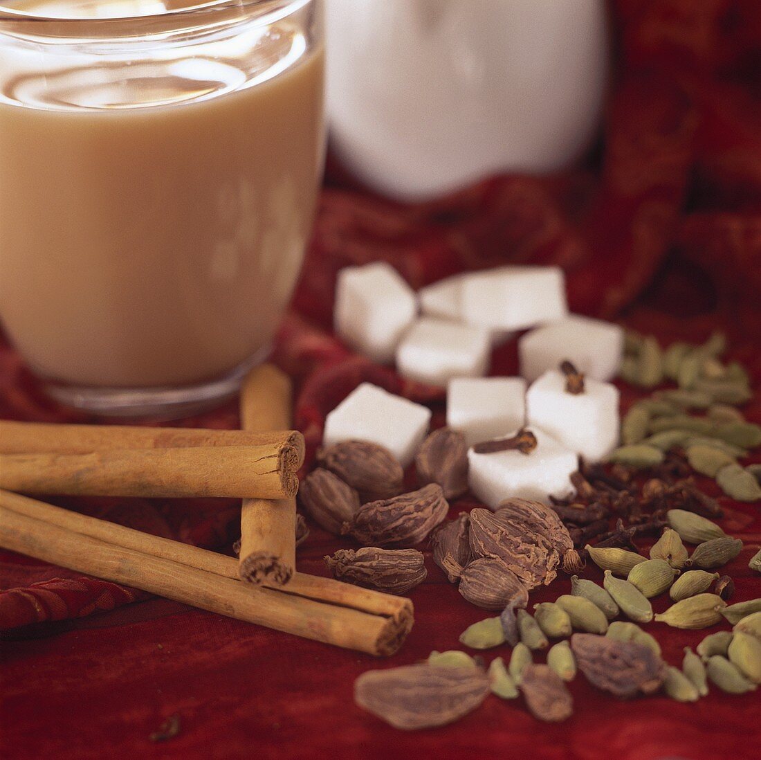 A glass of yogi tea, spices, sugar and milk jug beside it
