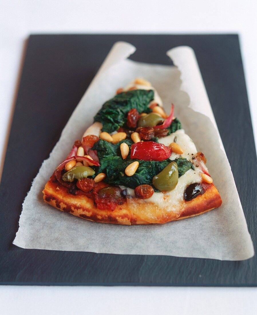 A piece of pizza with vegetables, cheese, pine nuts & raisins