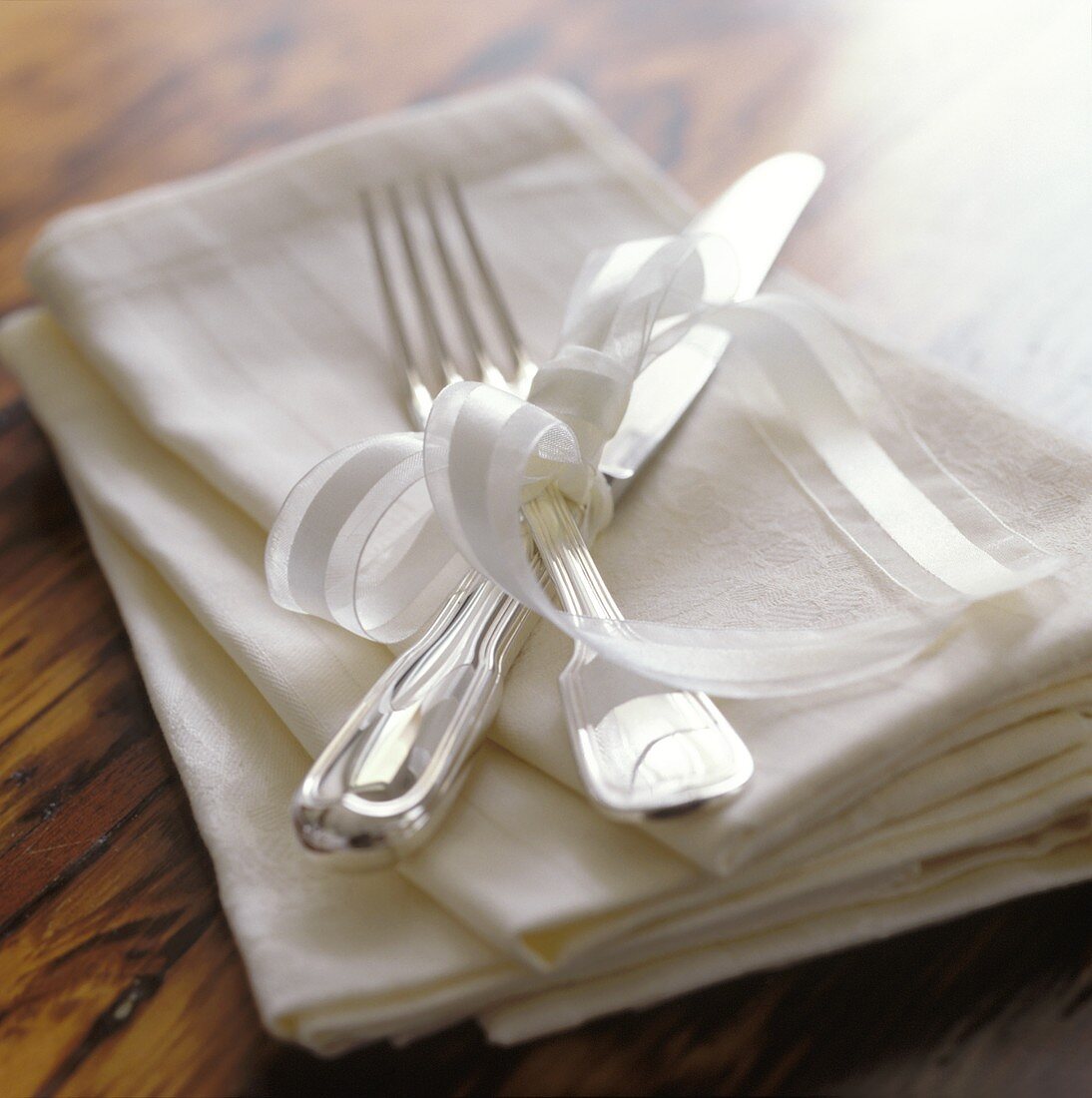 Silver cutlery with white bow on napkins