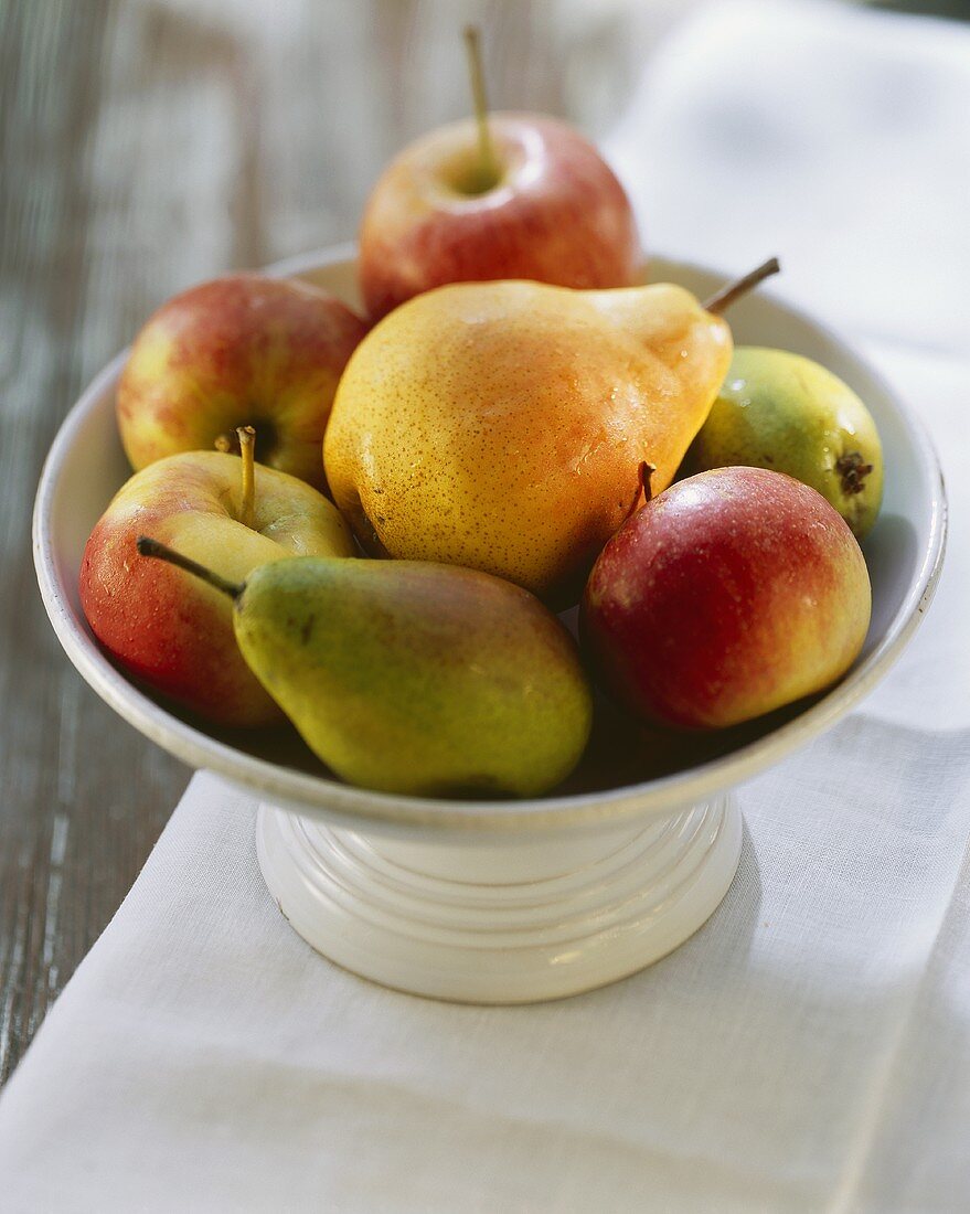 Apples and pears in a white bowl on a table