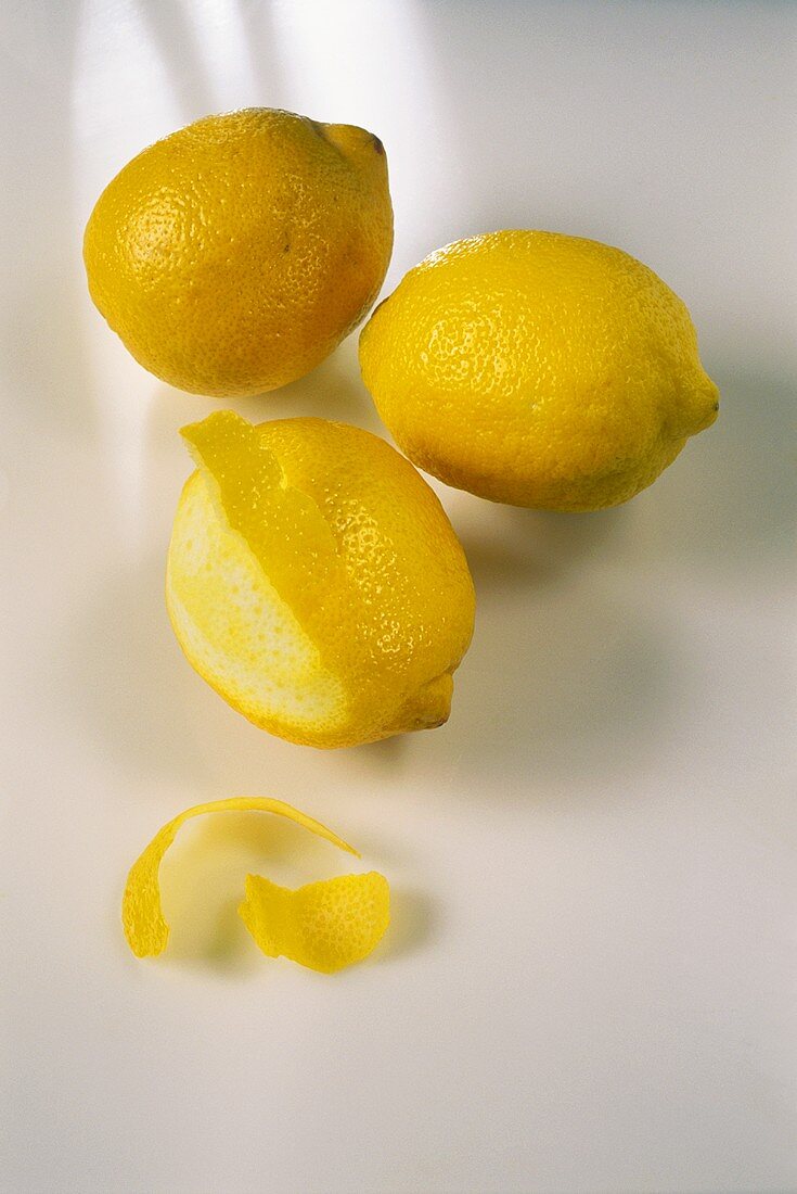 Zitronen, eine halb geschält, davor Schalenstücke