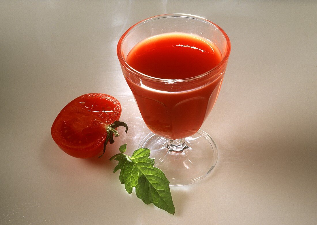 Ein Glas Tomatensaft, daneben halbe Tomate und Tomatenblatt