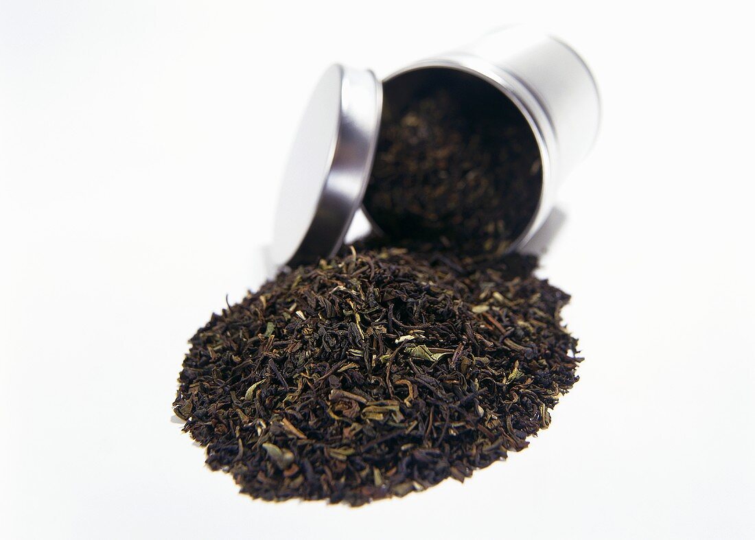 Schwarzer Tee fällt aus geöffneter runder Teedose