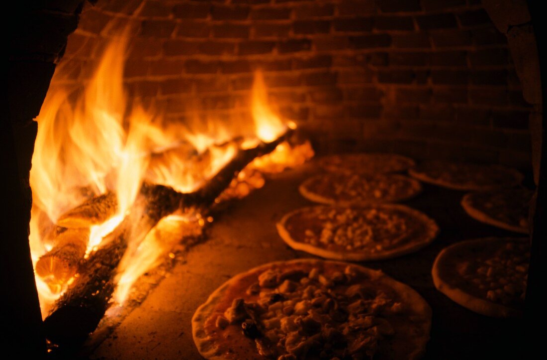 Pizzen im Pizzaofen mit Holzfeuer