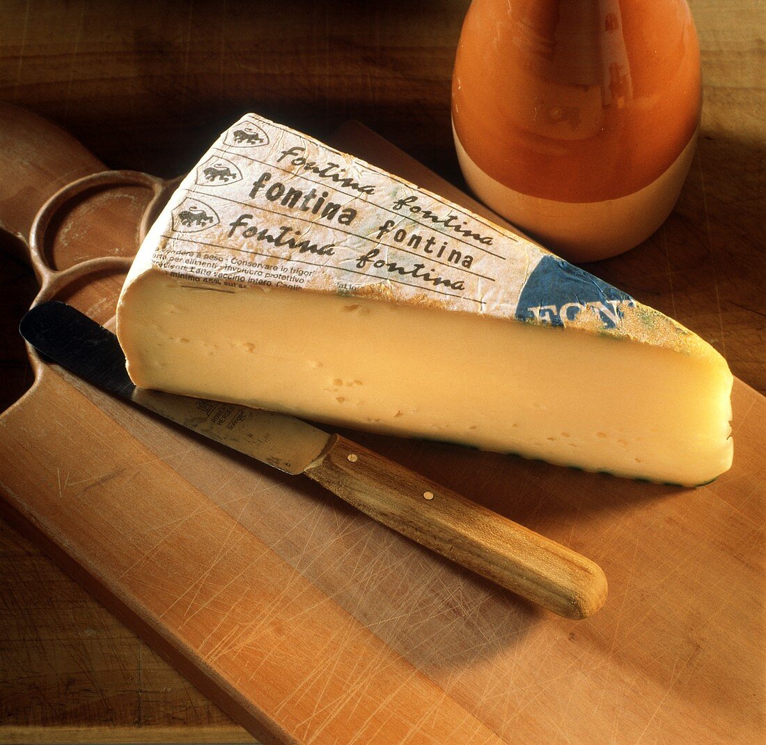 A piece of Fontina on a chopping board with knife
