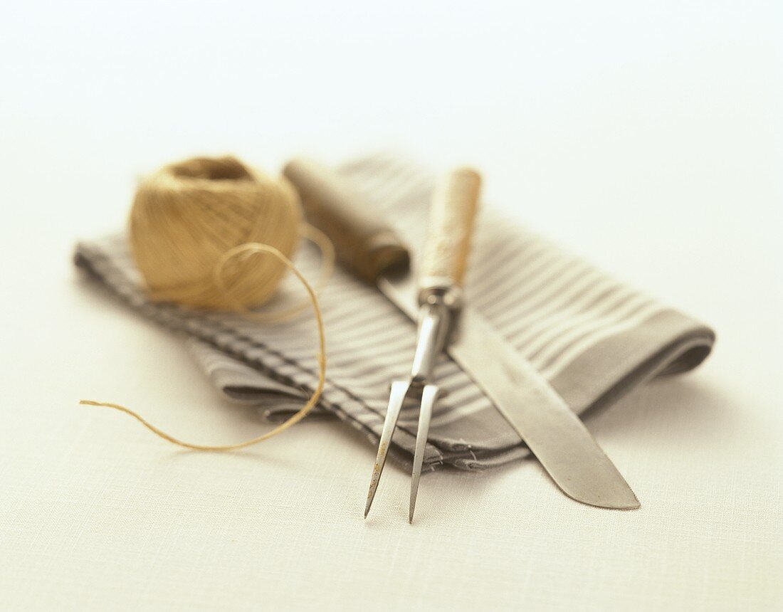 Meat fork, knife and kitchen string on kitchen cloth