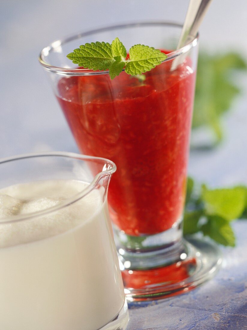 Red berry compote in dessert glass, cream in jug in front