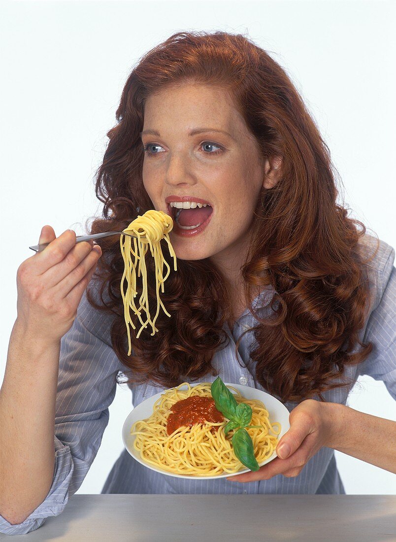 Red-haired woman eating spaghetti with tomato sauce