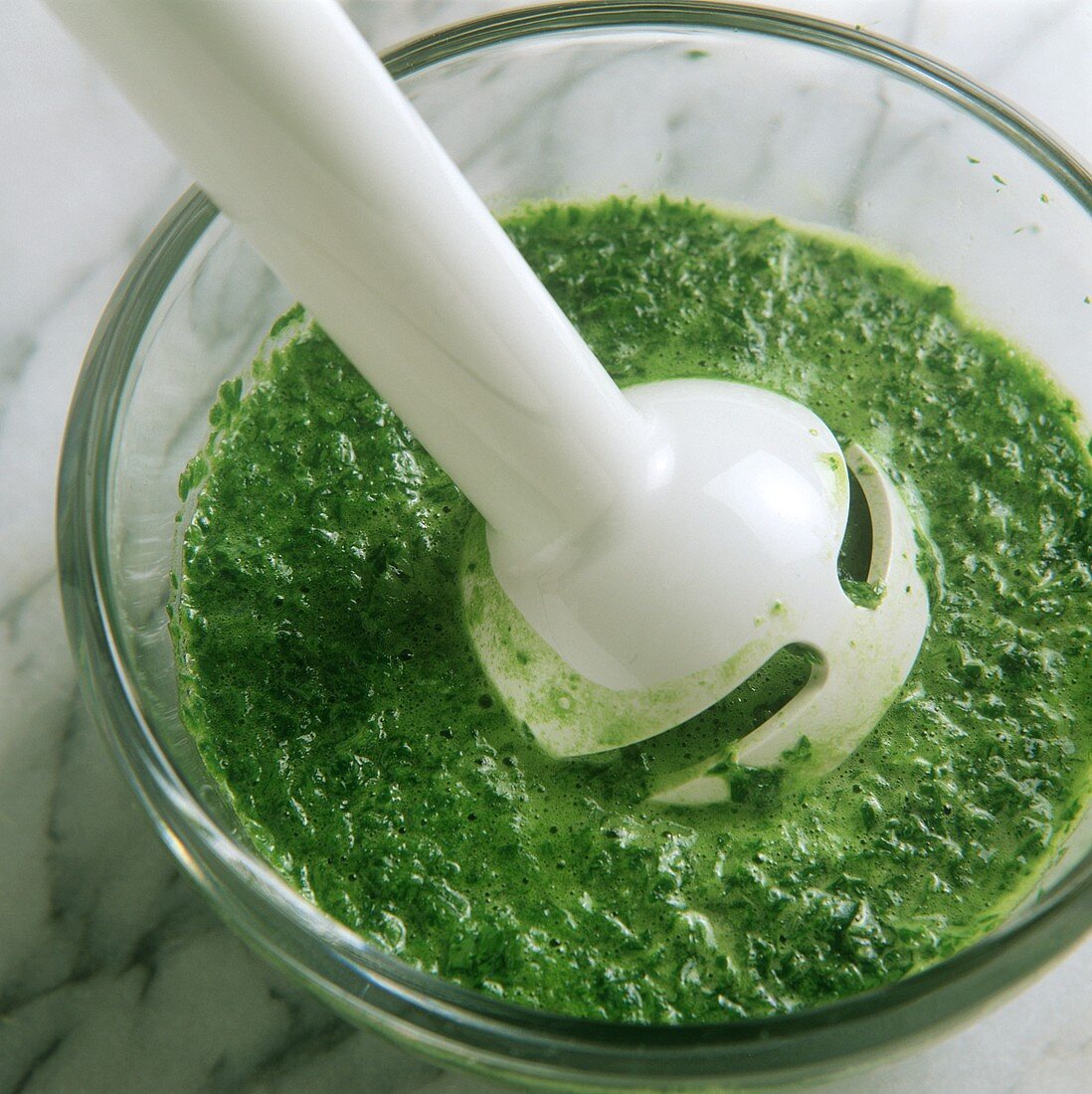 Mixing green herb sauce to a puree with hand blender
