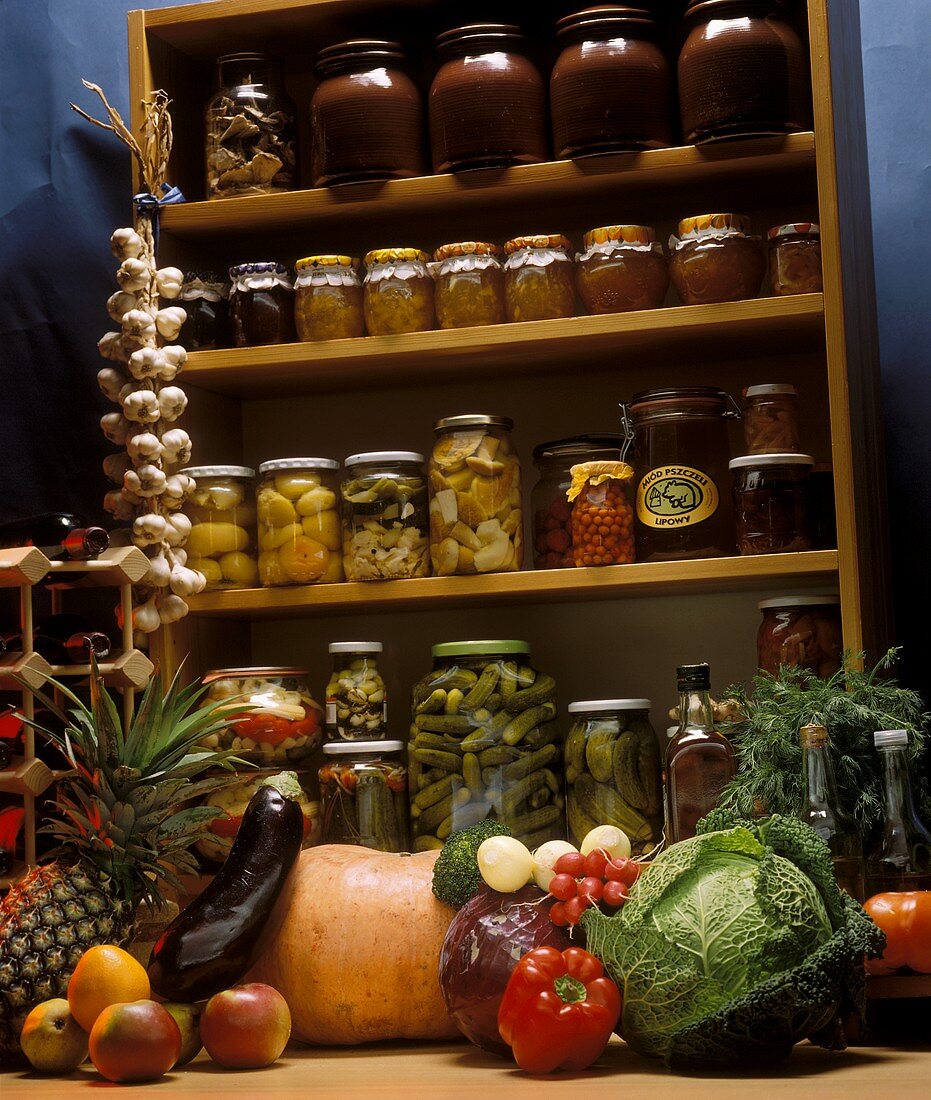 Pickles on a cellar shelf, vegetables and fruit in front