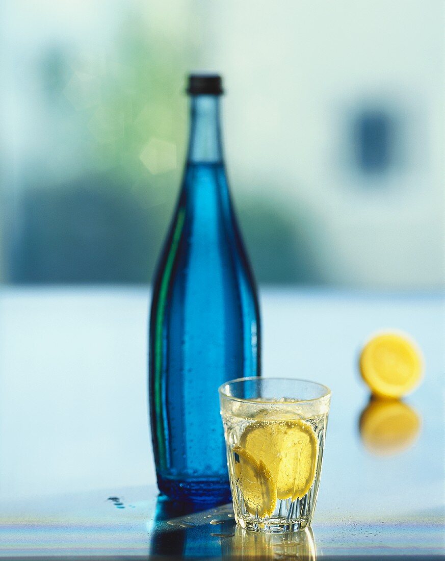 Blaue Wasserflasche & ein Glas Mineralwasser mit Zitronen