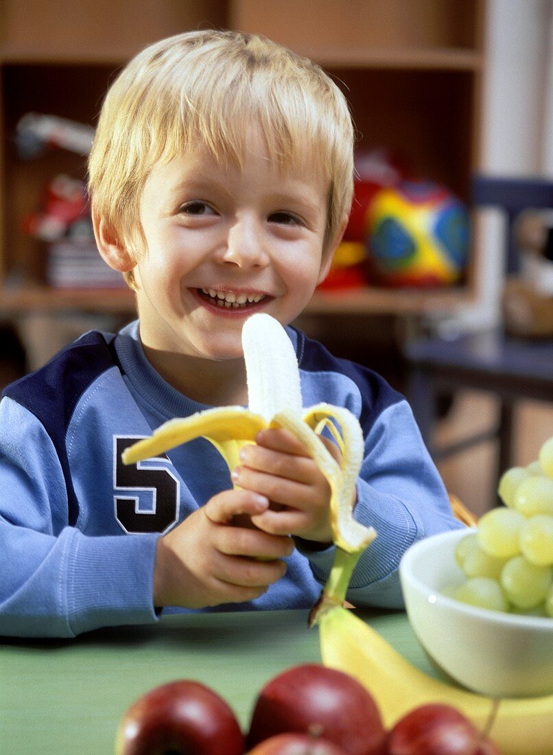 Small boy sitting at table with banana
