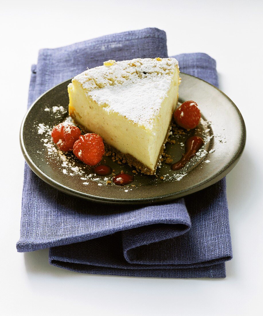 A piece of cheesecake with raspberries on dark plate