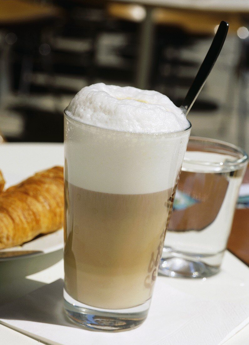 Latte macchiato, a glass of water and croissant