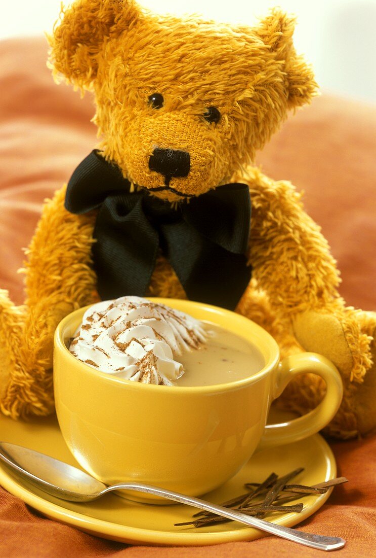 Eine Tasse Heiße Schokolade mit Sahne, dahinter Teddy