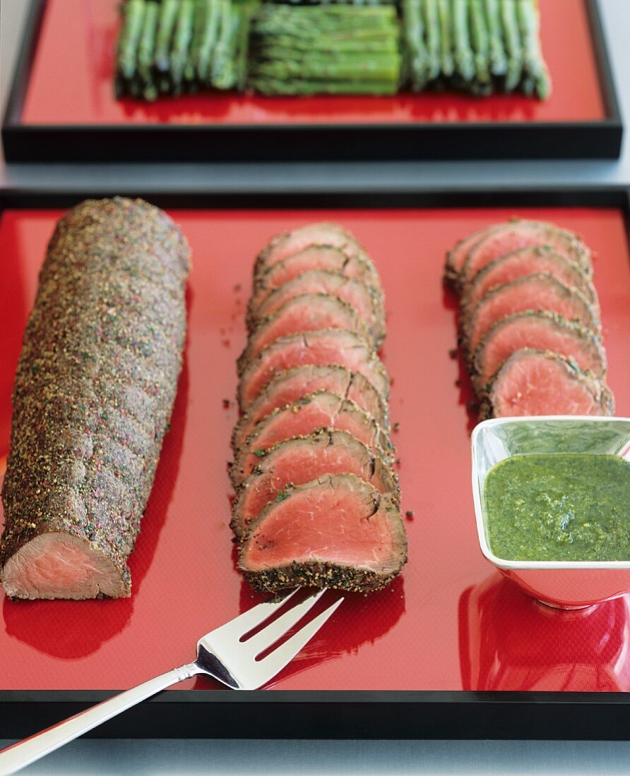 Roast beef in herb coating and a bowl of pesto