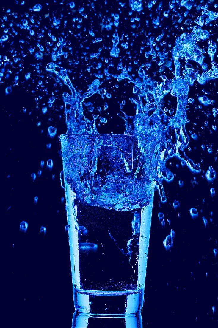 Blaues Wasser spritzt aus Wasserglas