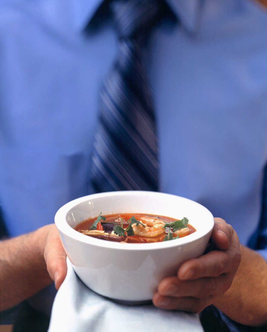 Mann hält Schälchen mit Tomaten-Orangen-Suppe mit Garnelen