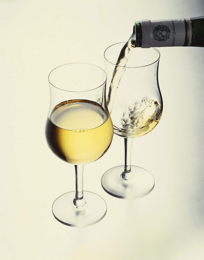 Weißwein in ein Glas einschenken, gefülltes Glas davor