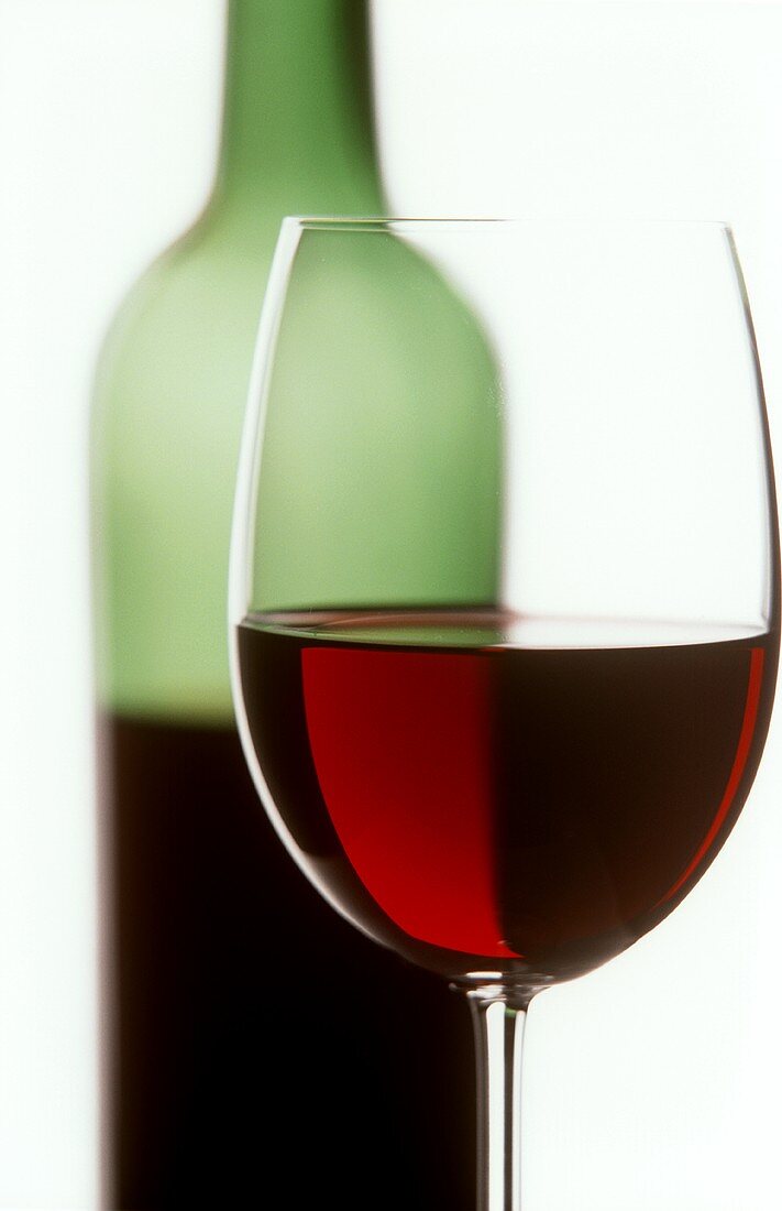 Red wine glass with half-full wine bottle in background
