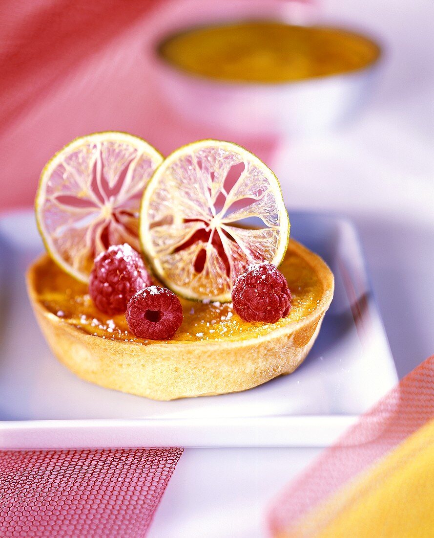 Lemon tartlet garnished with lemon slices and raspberries