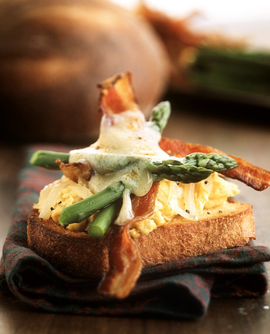 Slice of bread with scrambled egg, bacon, asparagus & cheese