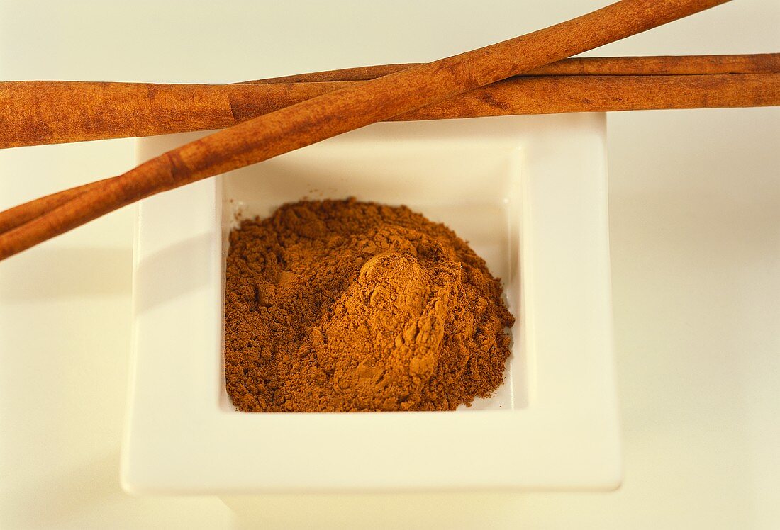 Ground cinnamon in a bowl and cinnamon sticks